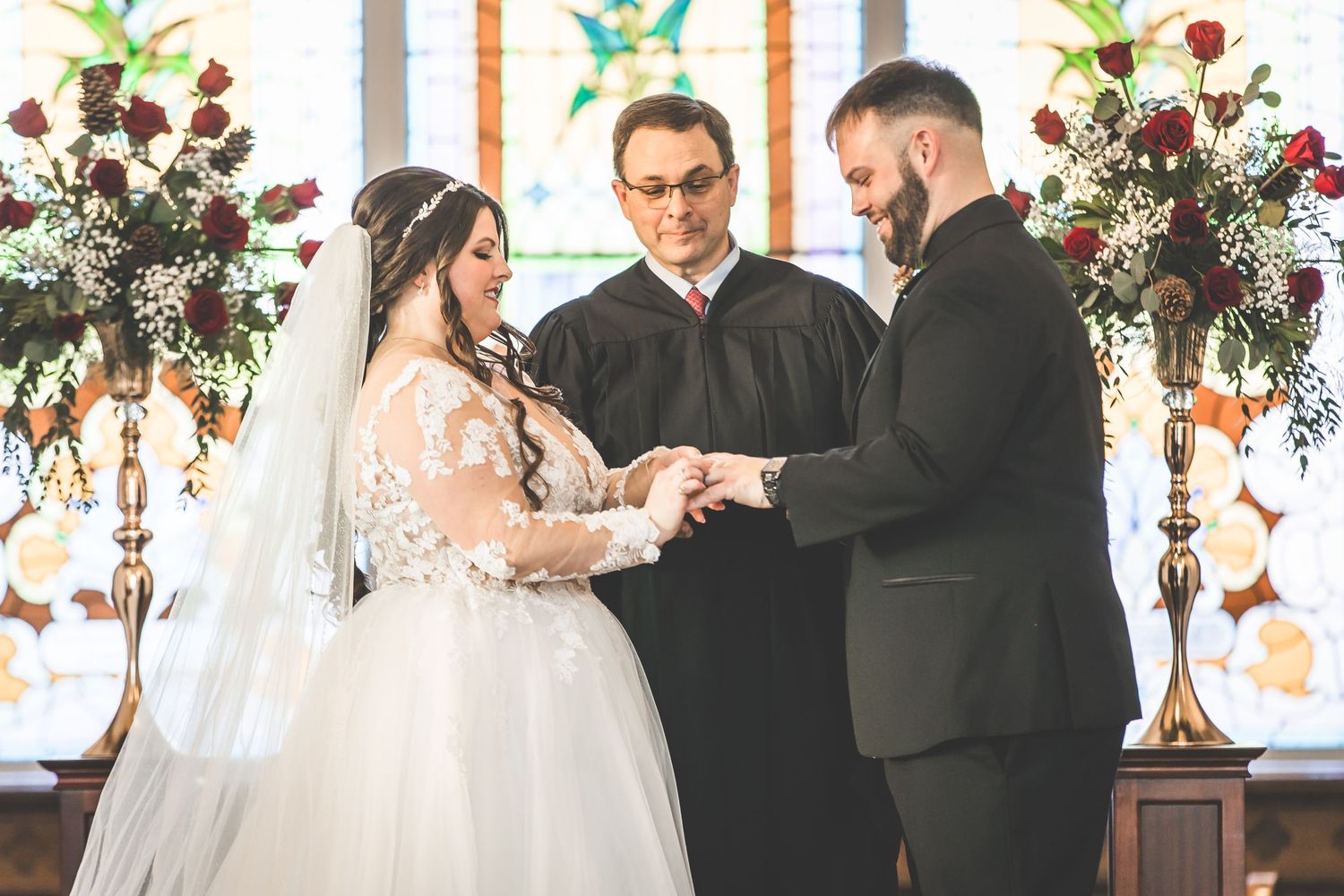 Wedding ceremony in a church with stained glass windows and floral decorations.