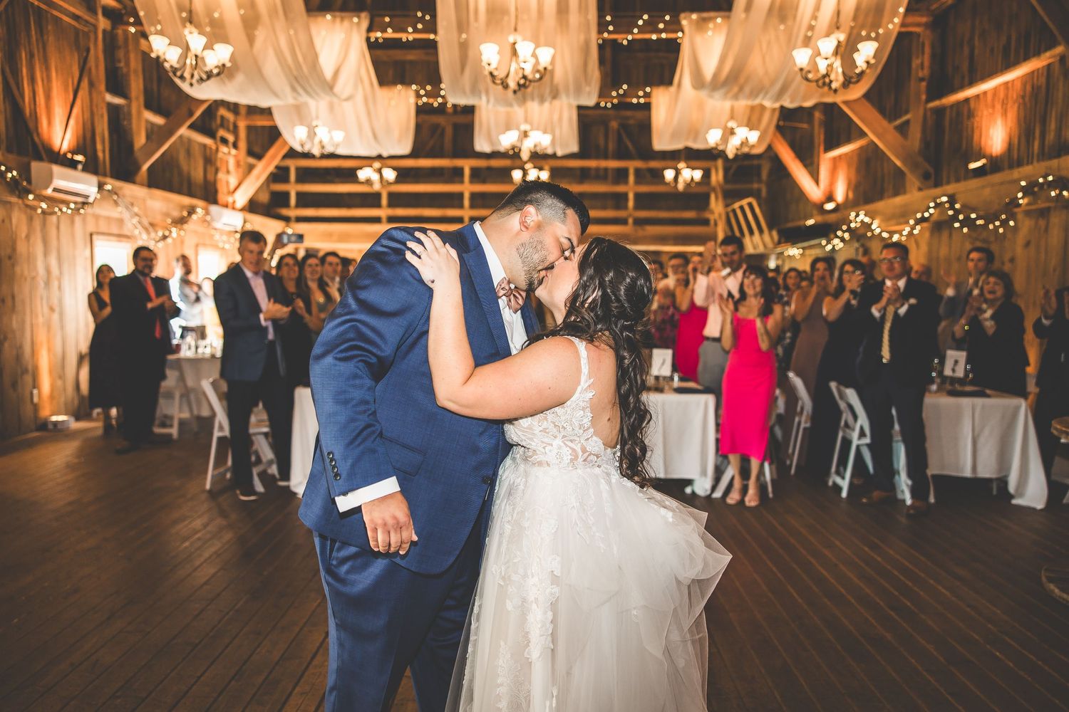 Romantic first dance at a rustic barn wedding reception with warm lighting and chandeliers.