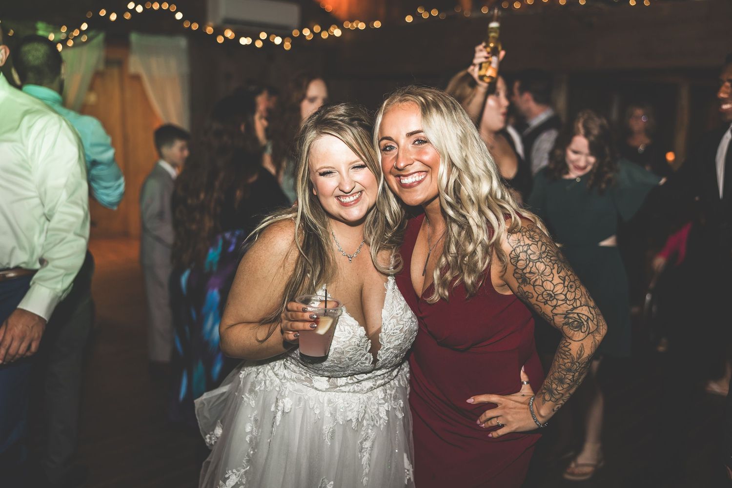 Wedding guests dancing and celebrating in a rustic venue with string light decorations.