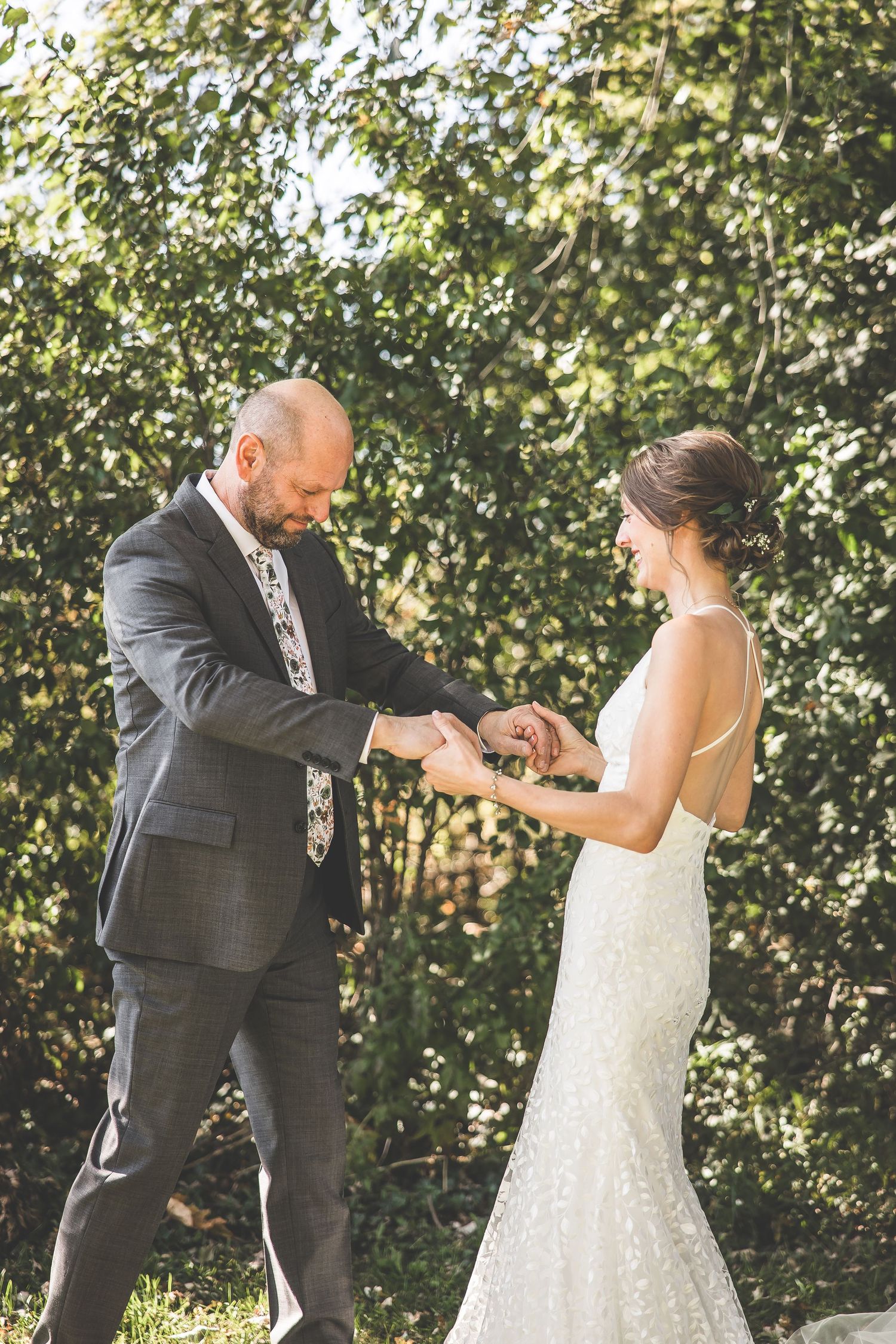 An emotional ring exchange moment during an outdoor wedding ceremony with natural sunlit backdrop.