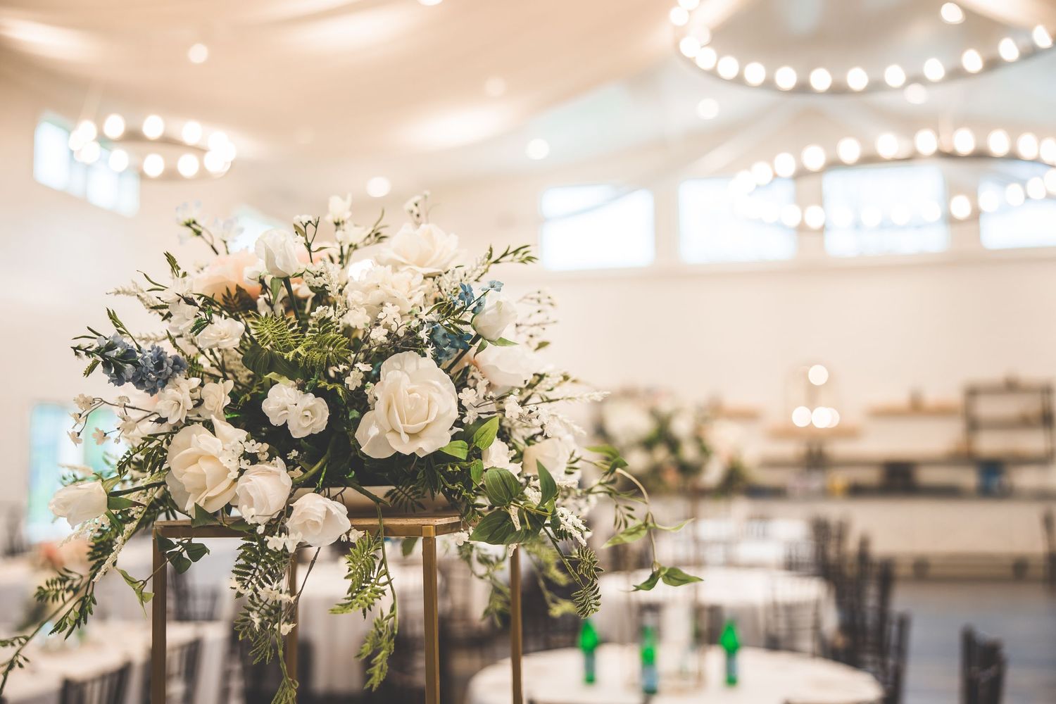 An elegant white floral centerpiece arrangement under crystal chandeliers in a reception venue.