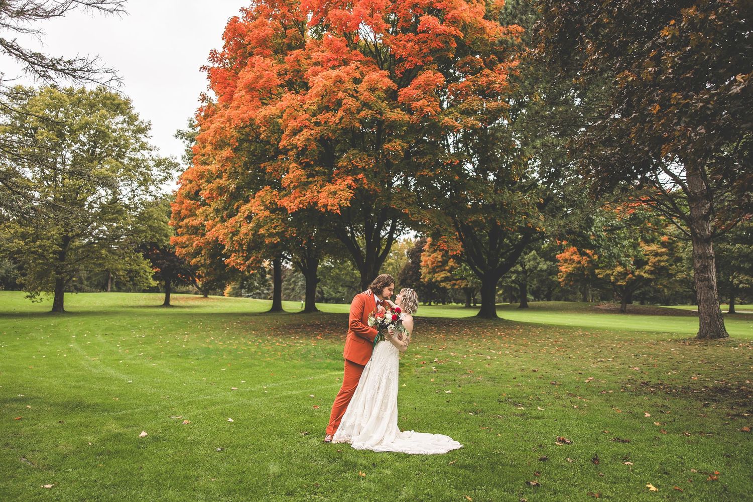 Wedding photos captured against brilliant orange fall foliage in a serene park setting.