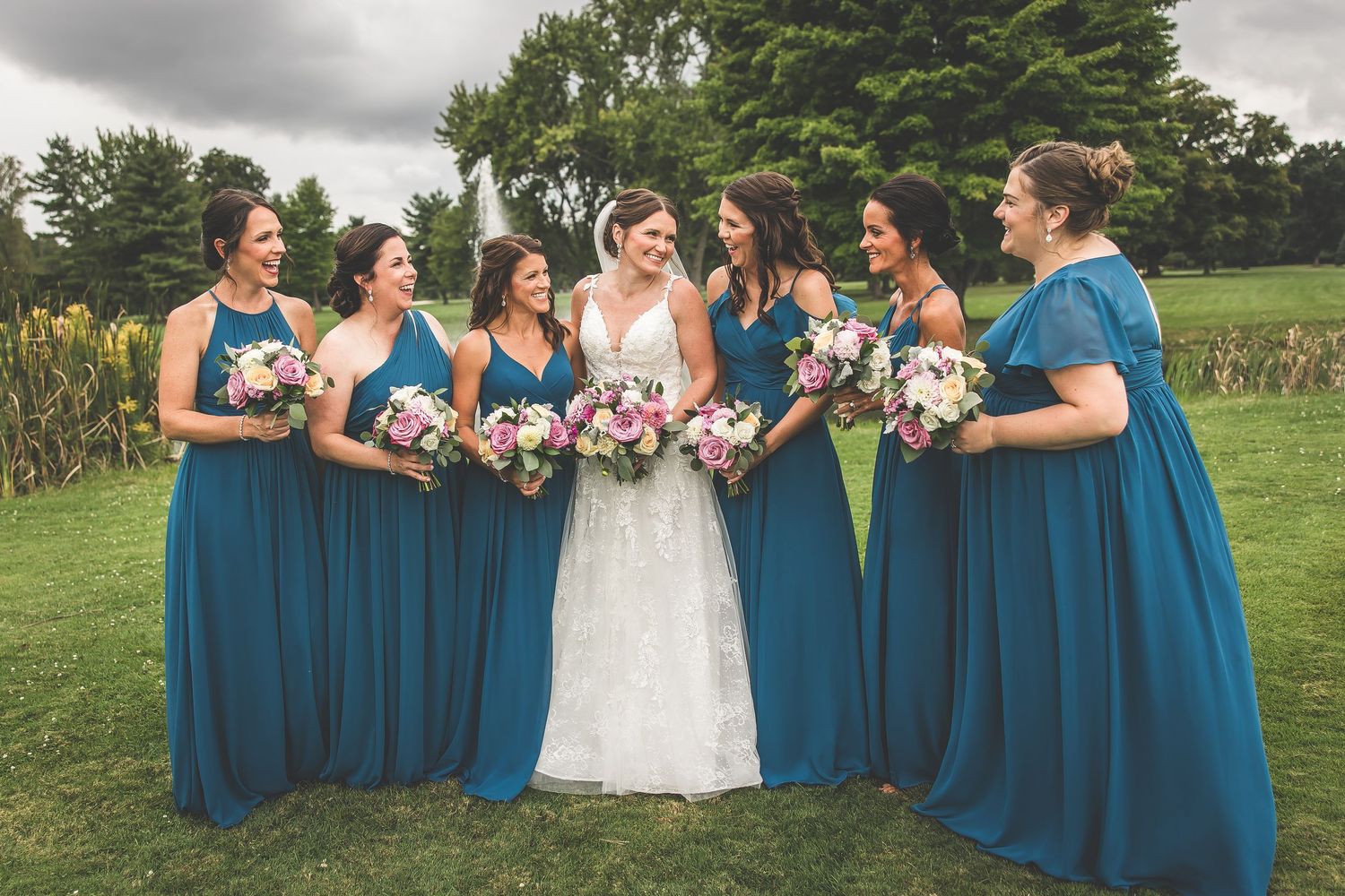 Bridesmaids in vibrant blue dresses pose with bouquets on green lawn.