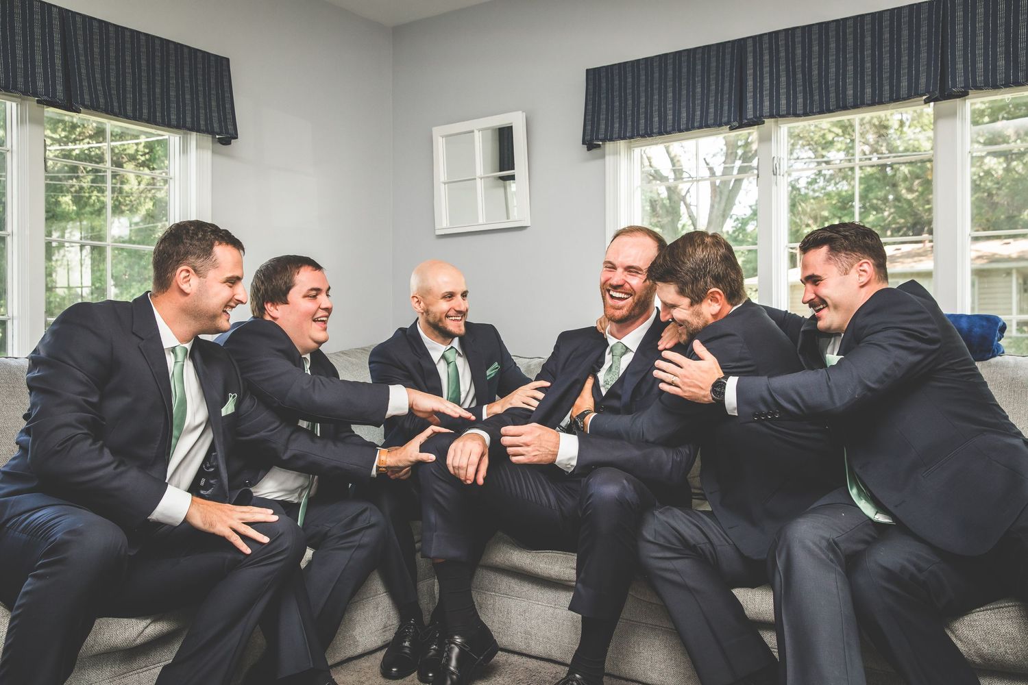 Groomsmen in dark suits pose playfully in indoor setting.