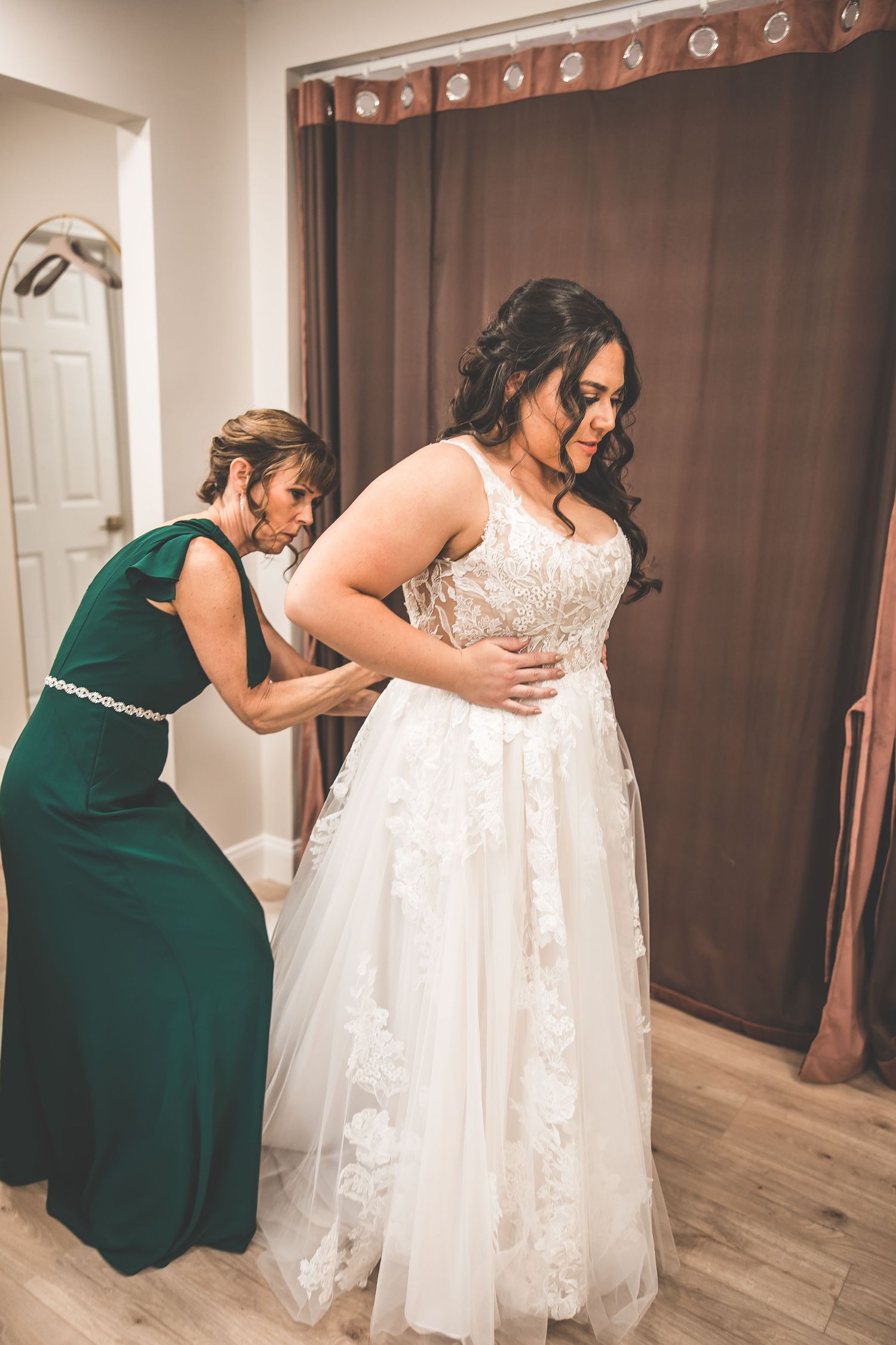 Helpers assist with adjusting an elegant lace wedding gown during final preparations.