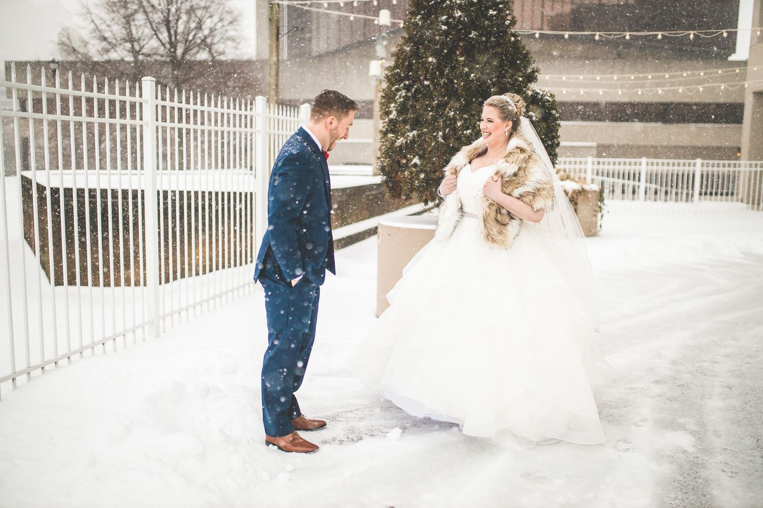 Wedding couple posing in snowy outdoor setting with white fencing.