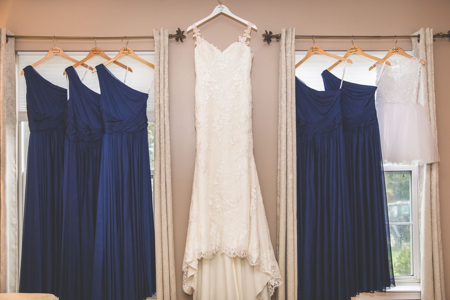 Row of navy blue bridesmaid dresses and white wedding gown hanging on display.