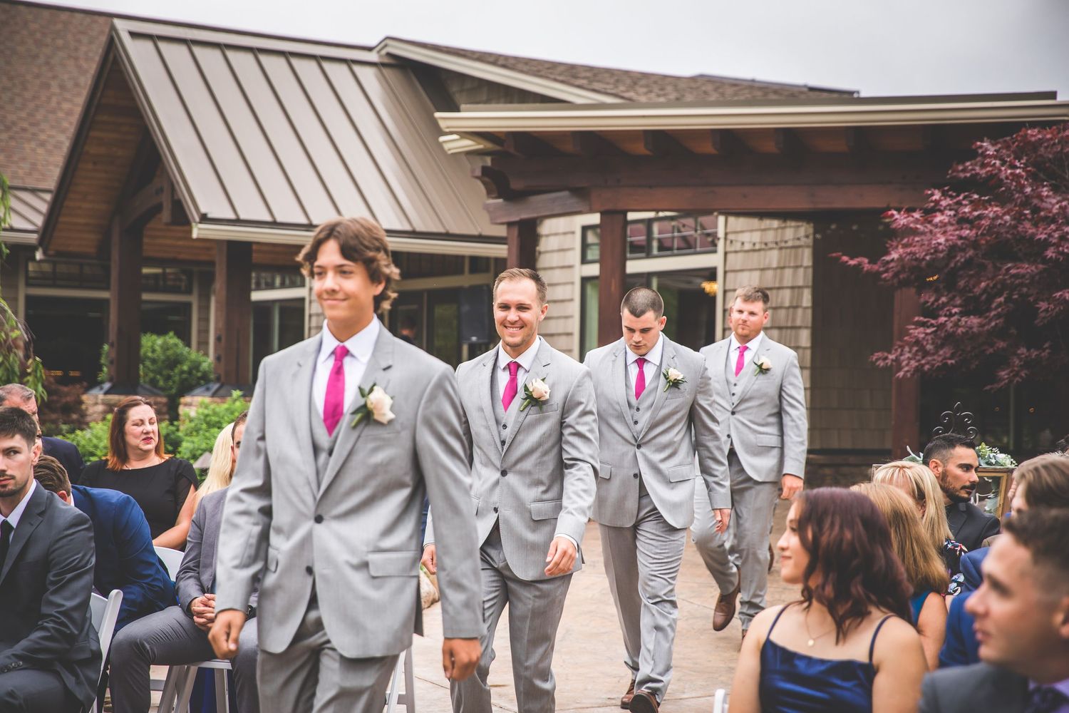 Wedding party members gather outside rustic venue wearing coordinated gray and purple attire.