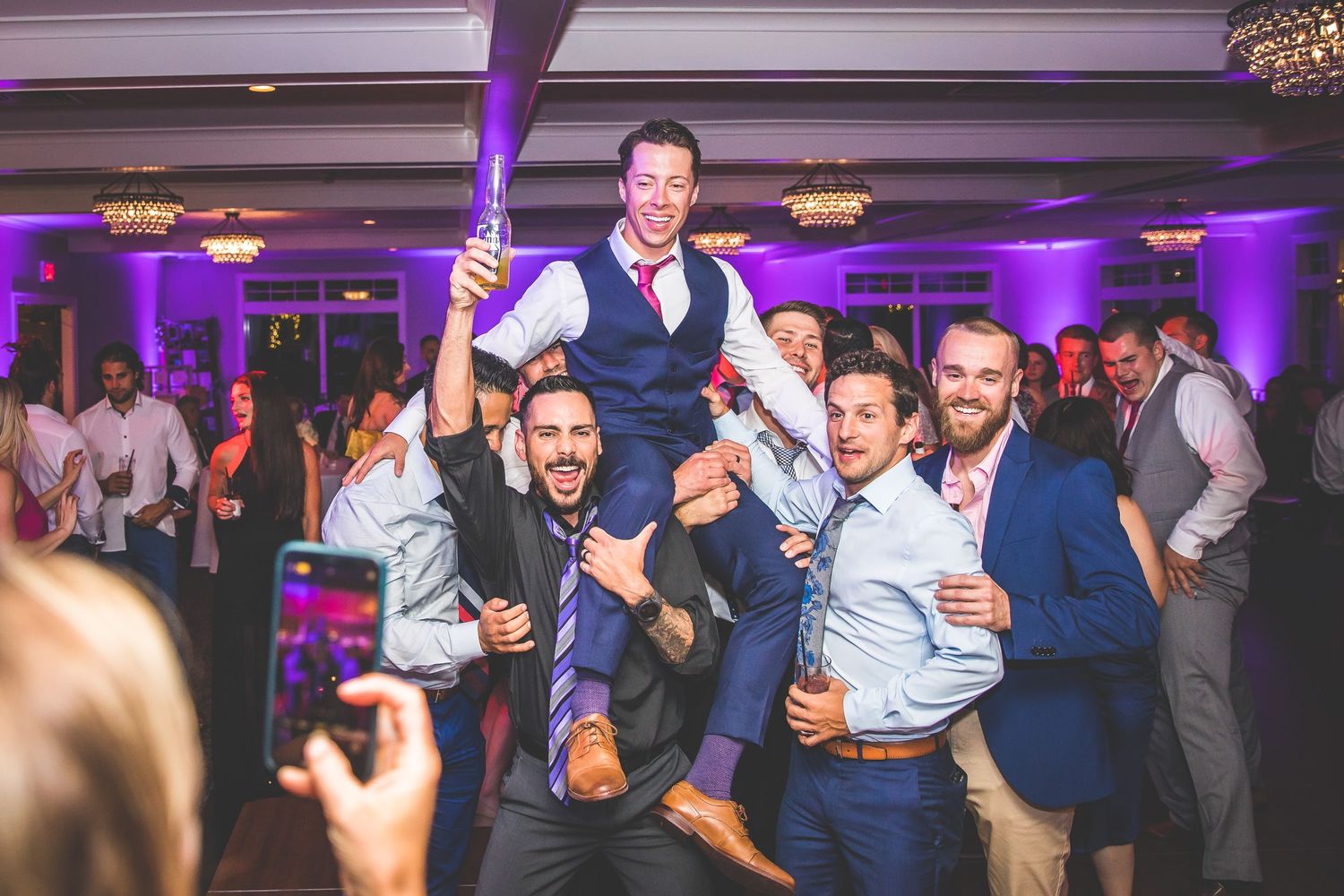 Wedding party dancing in an elegant ballroom venue with dramatic purple lighting effects.