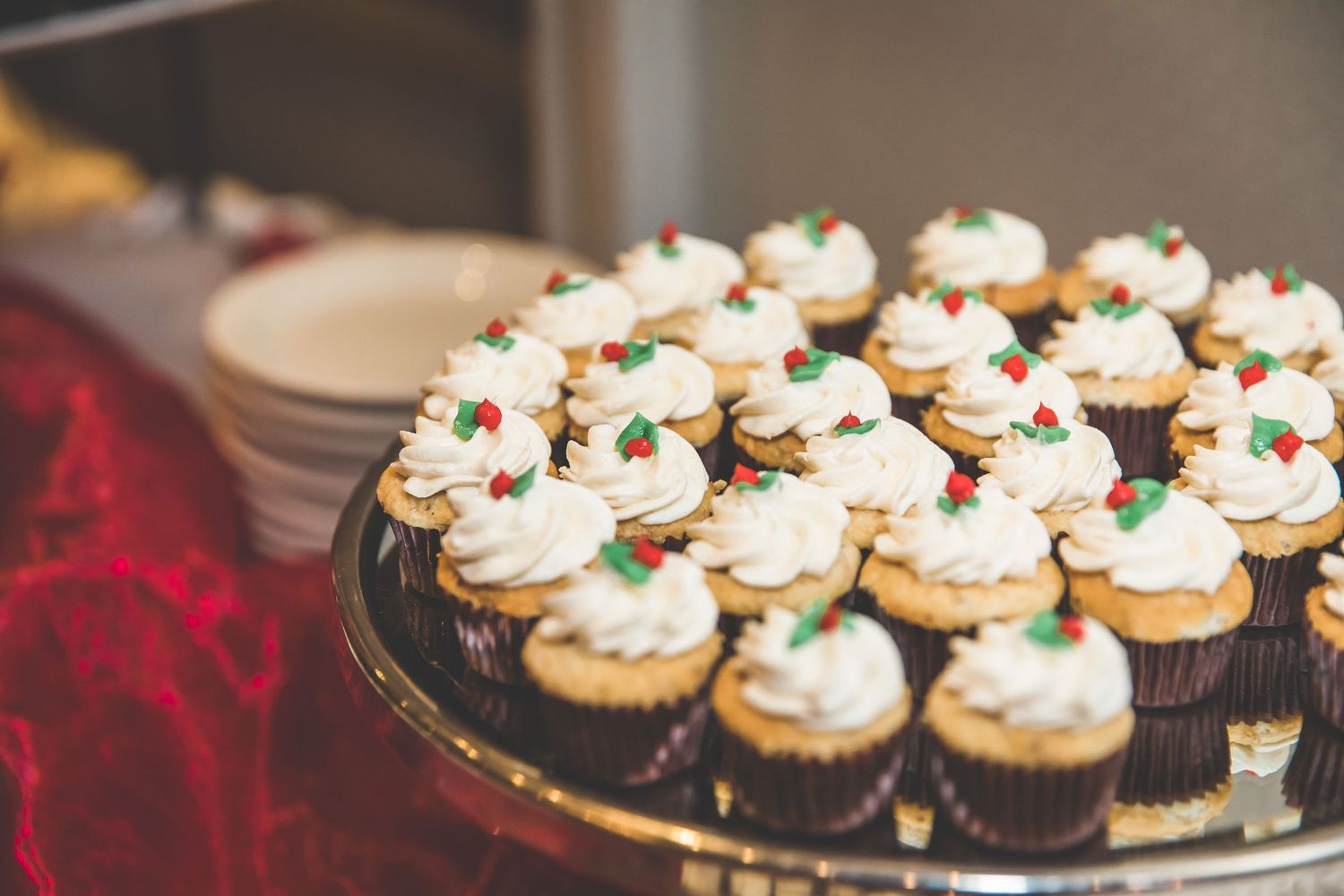 Beautifully decorated cupcakes with white frosting and small decorative toppings displayed on silver platters.