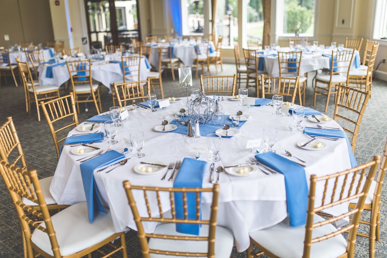Reception venue set with blue and white table settings and wooden chairs.