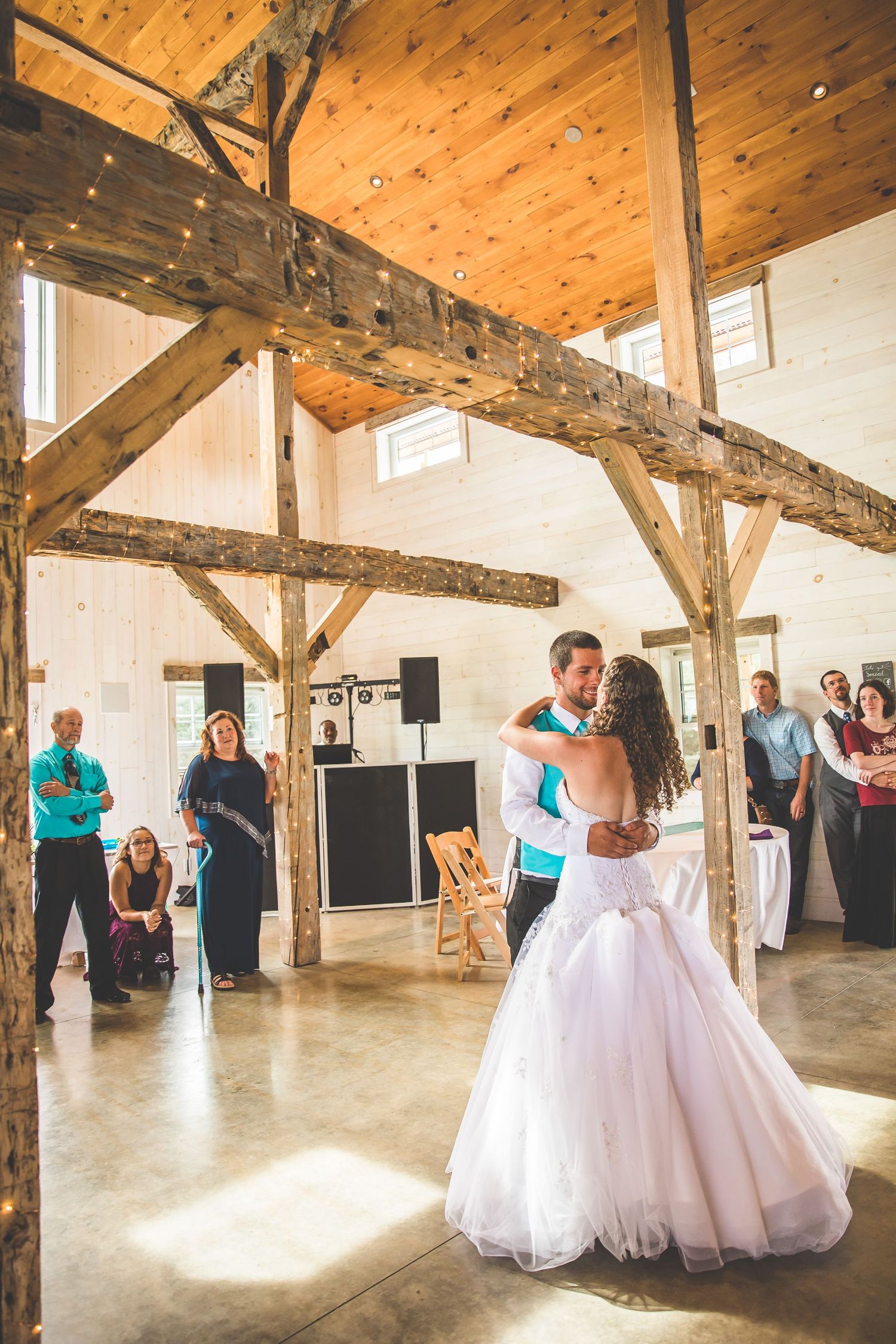 A couple dances in a rustic barn venue with exposed wooden beams and natural lighting.