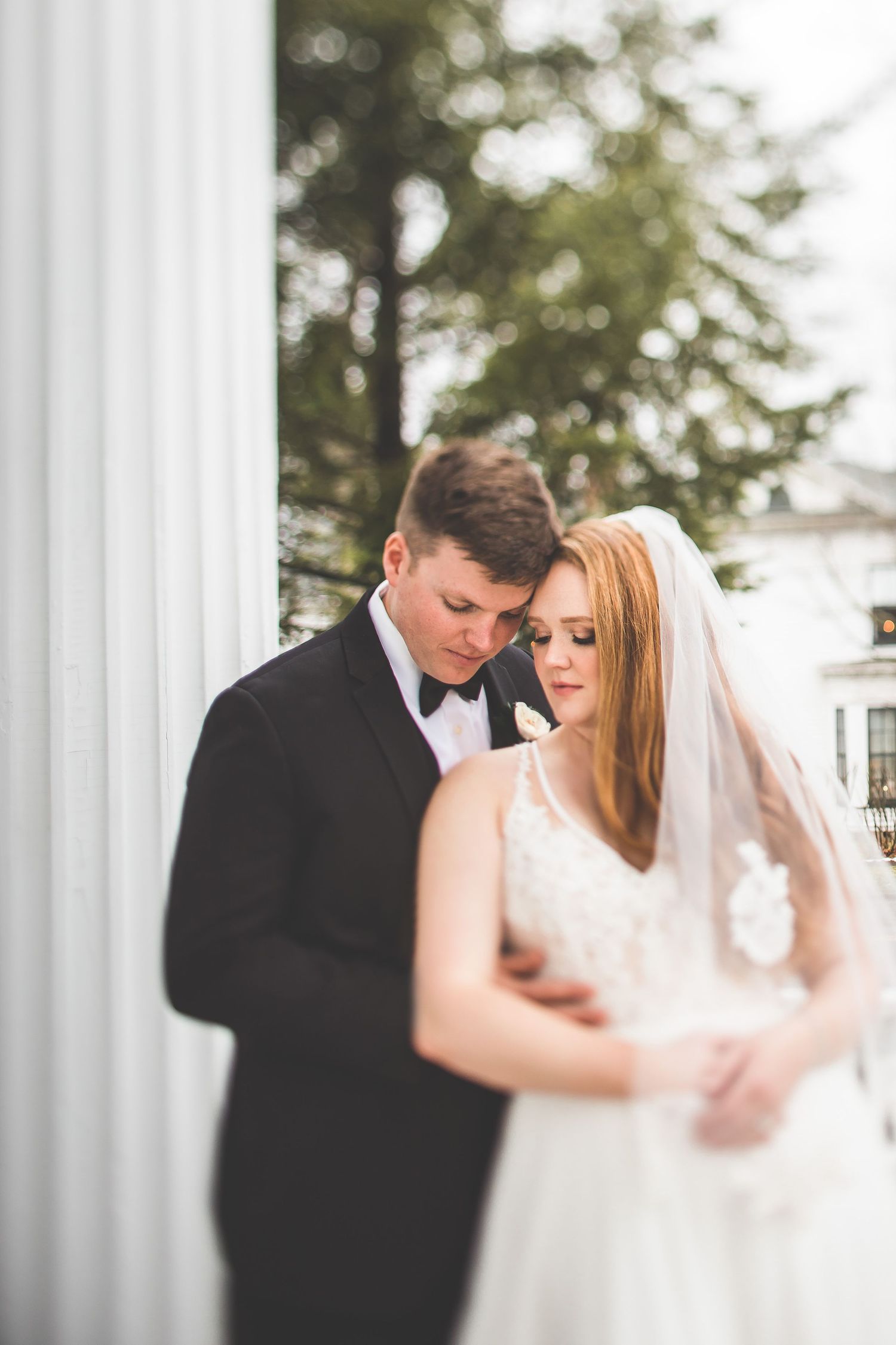 Romantic wedding portrait between classic white columns in an outdoor setting.