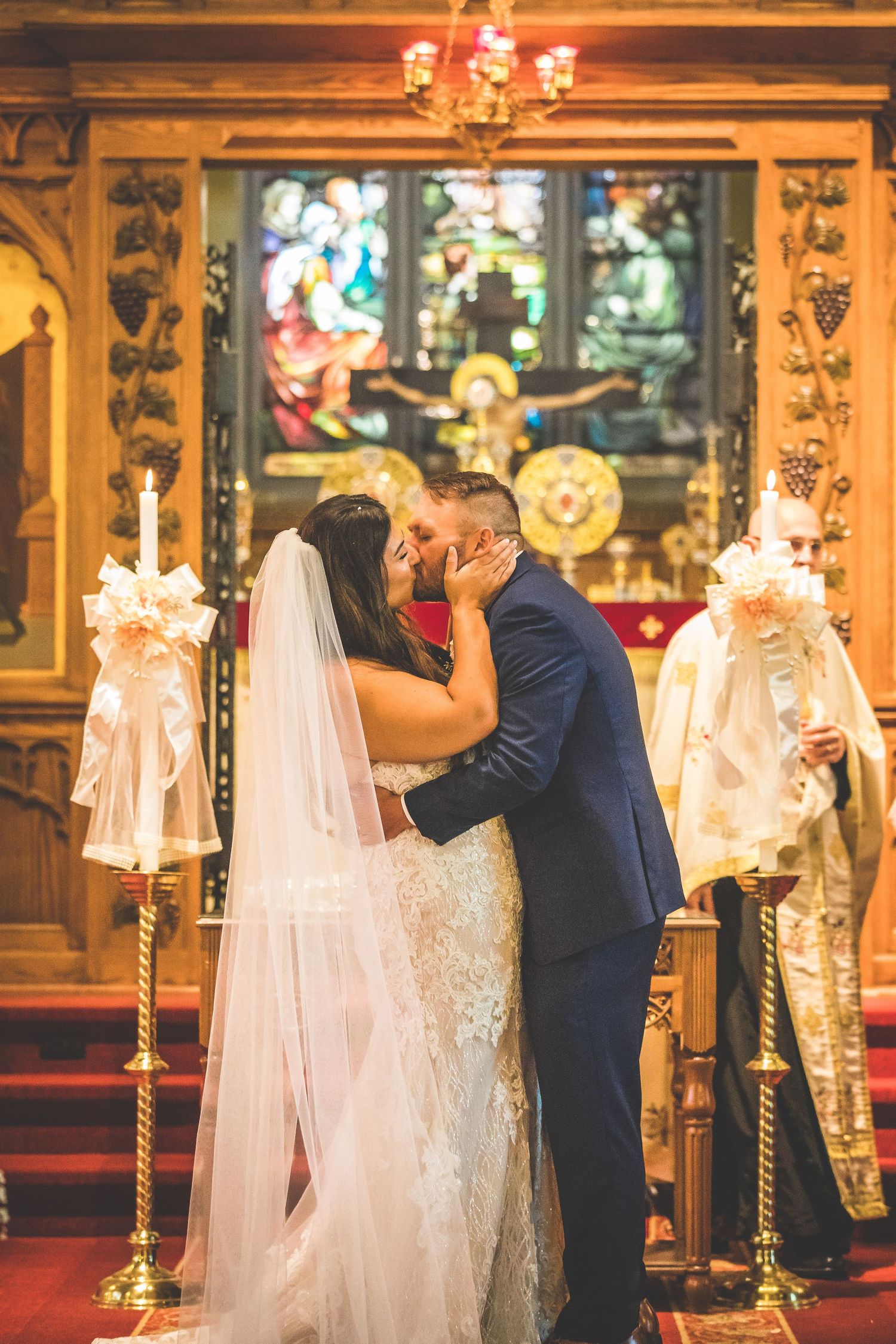 Romantic wedding ceremony moment in front of an ornate church altar with stained glass windows.