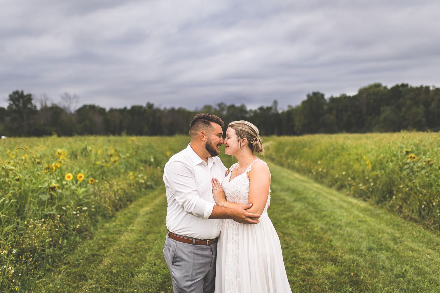 Couple embracing in a field of wildflowers on a cloudy day.