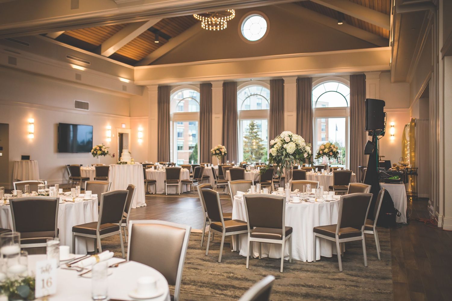 Spacious wedding reception venue with white tablecloths and elegant lighting fixtures.
