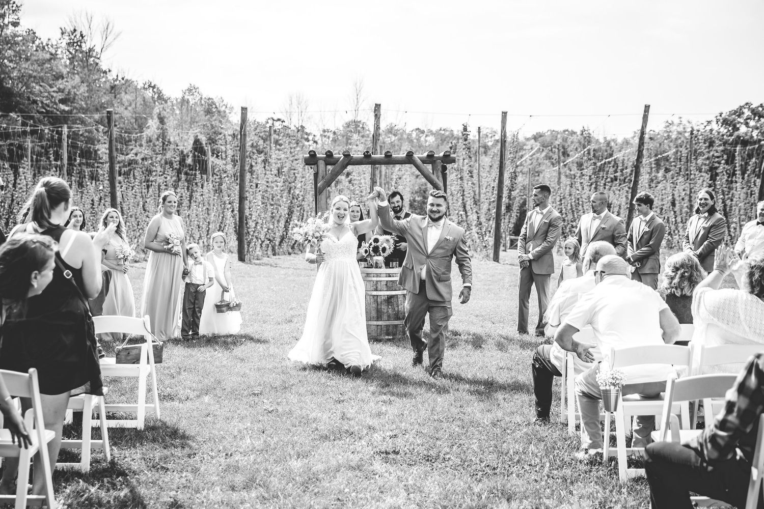Black and white panorama of garden wedding ceremony with wooden pergola and guest seating.