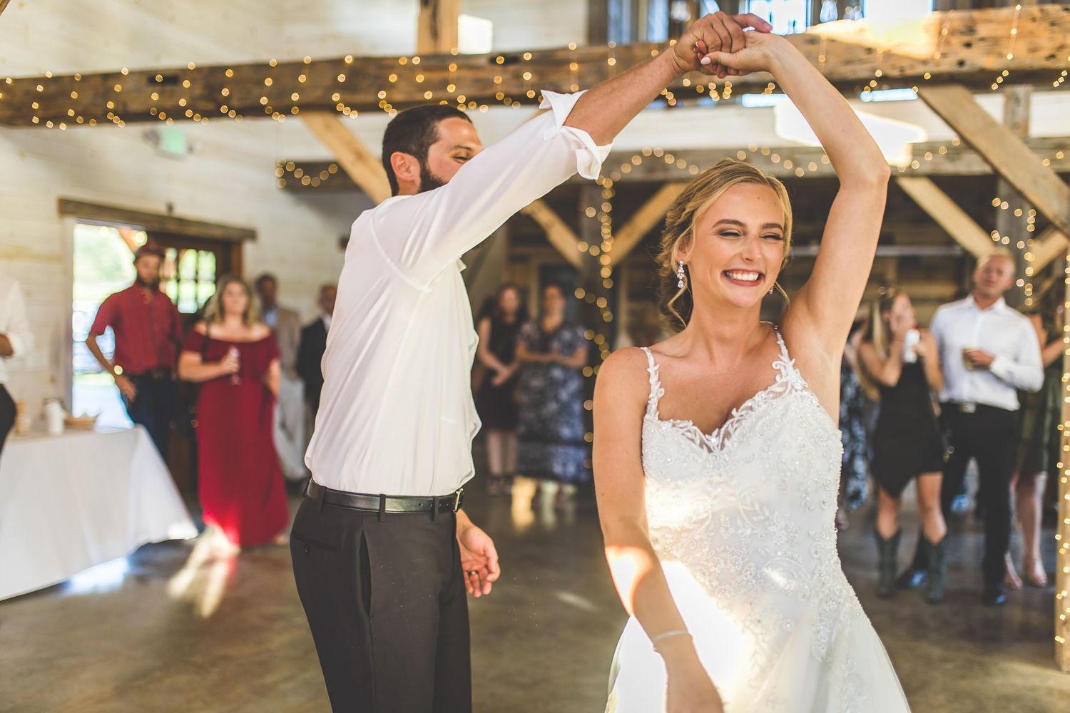 Couple performs an energetic dance move during their wedding reception in a barn venue.