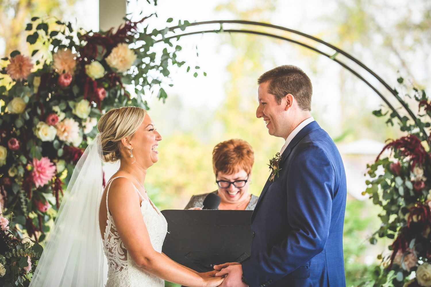 Outdoor wedding ceremony under an arch adorned with pink and white flowers.