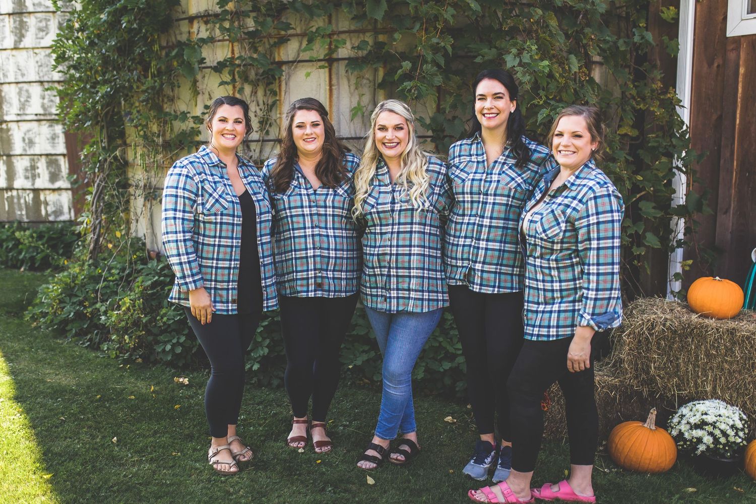 Wedding party in coordinating blue plaid shirts posing outdoors with pumpkin decorations.