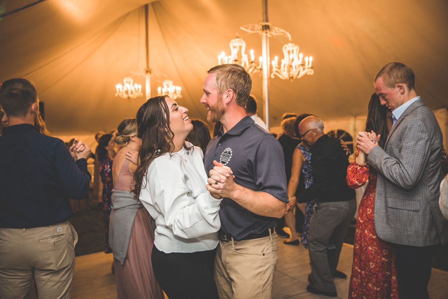 Wedding celebration with guests dancing under warm lighting in an elegant tent venue.