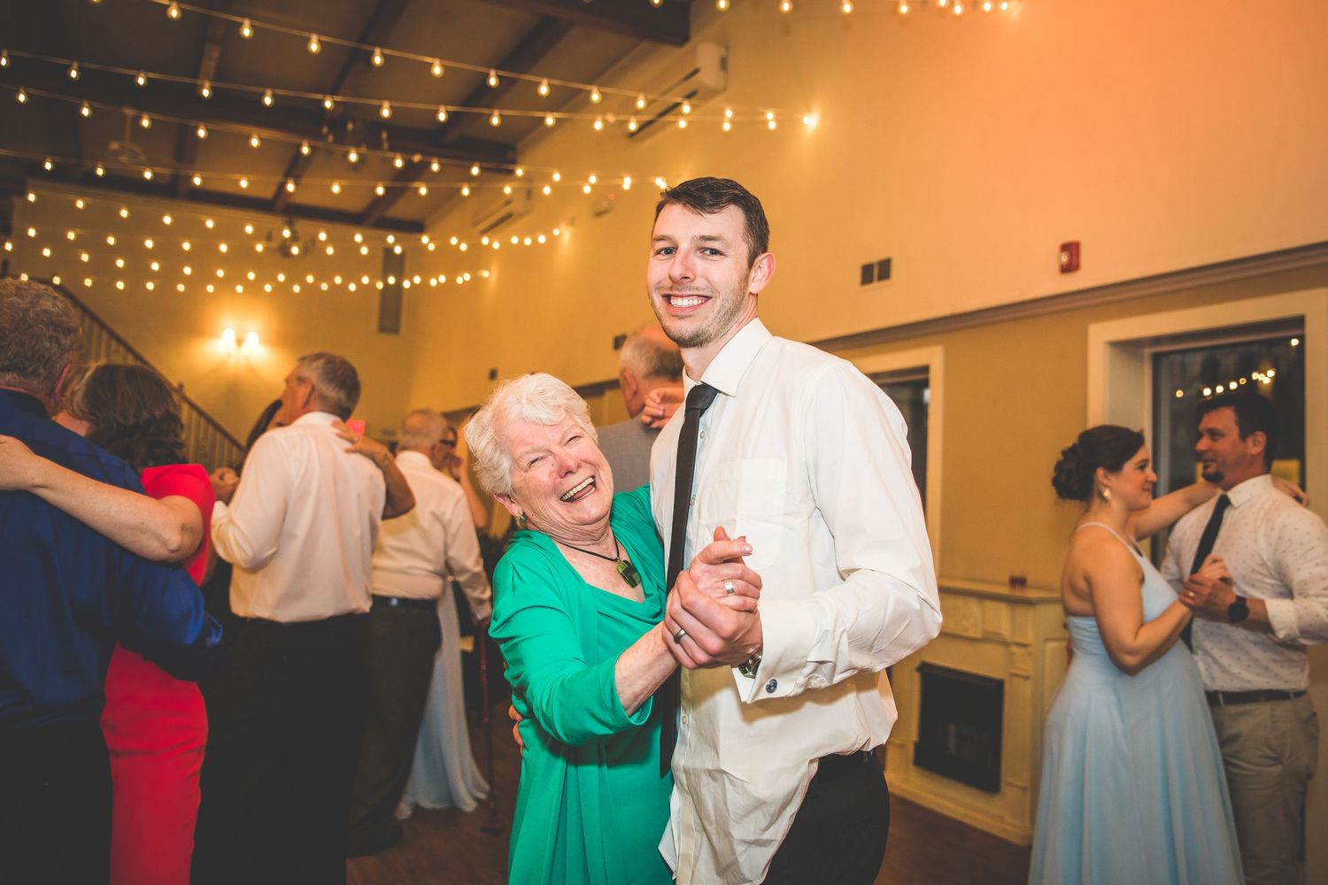 Couples dance under warm string lights during an evening wedding reception.
