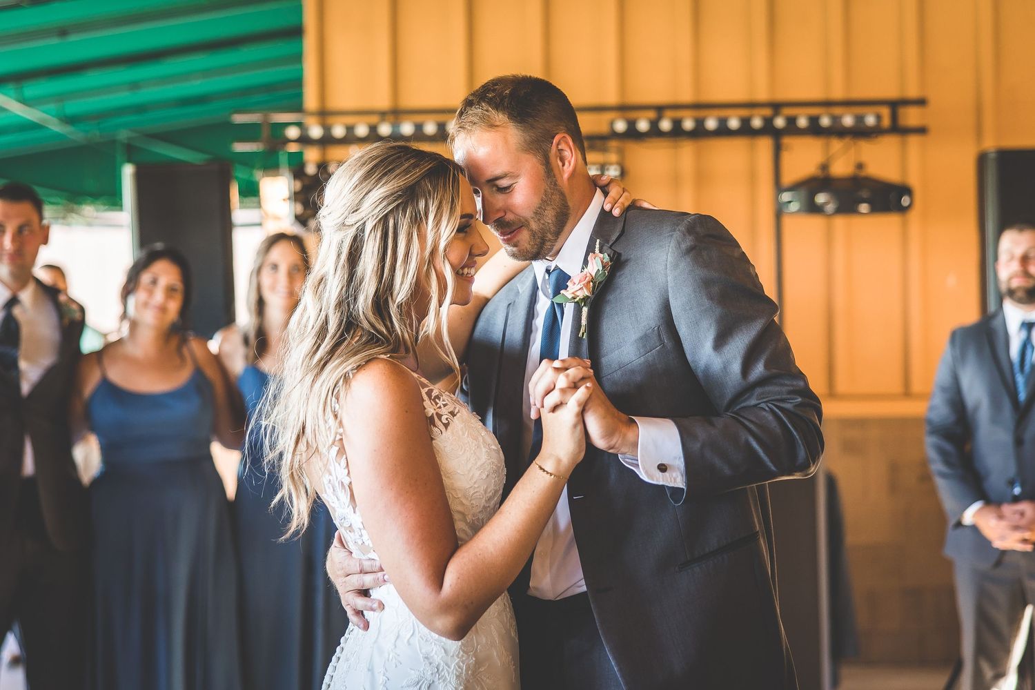 A couple dances together at their wedding reception in a venue with orange walls and string lights.