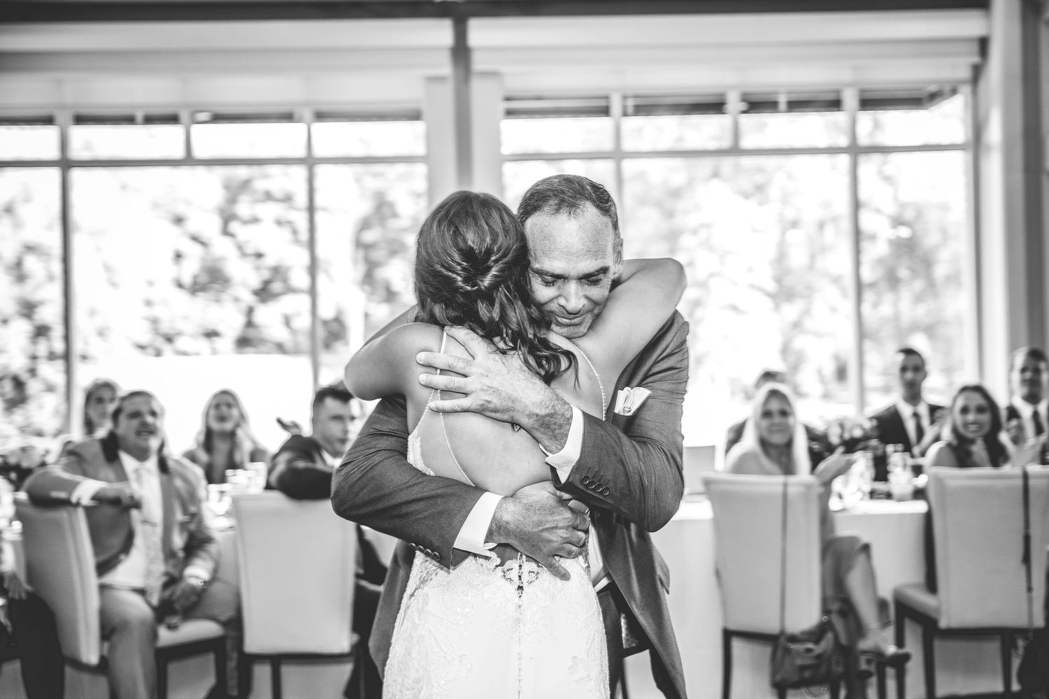 Wedding guests watch as couple performs their first dance in sunlit reception venue.