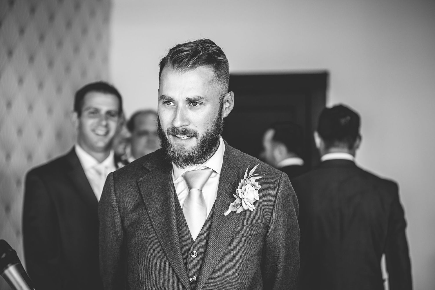 Wedding party members entering a reception venue with flowing curtains and hardwood floors.