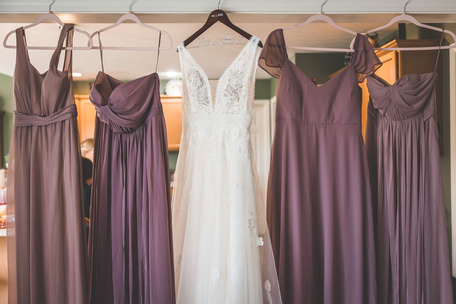 Purple bridesmaid dresses and white wedding gown hanging on display.