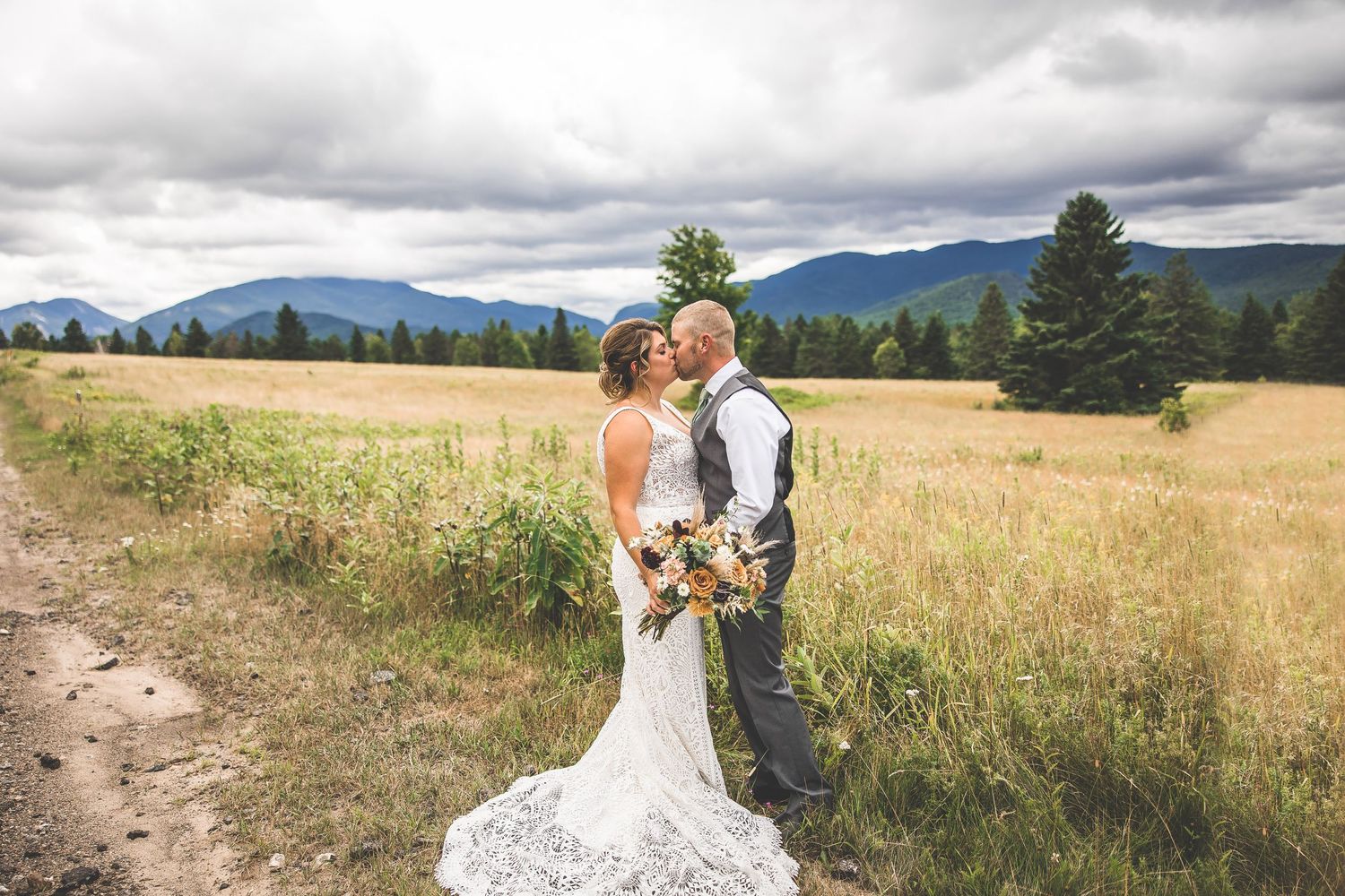 Newlyweds posing in a natural field setting with mountain landscape.