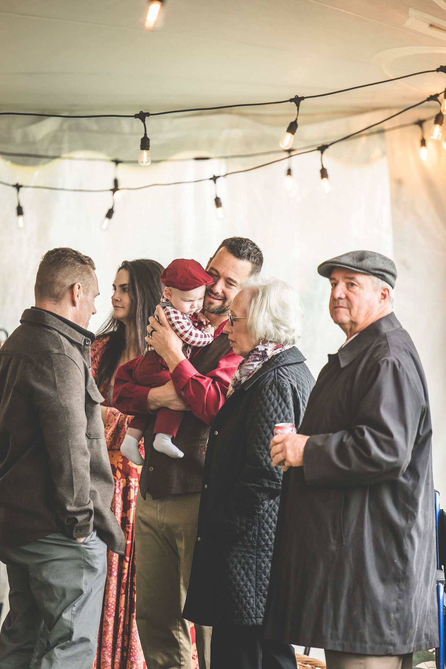 Wedding guests socialize under string lights at an indoor reception.