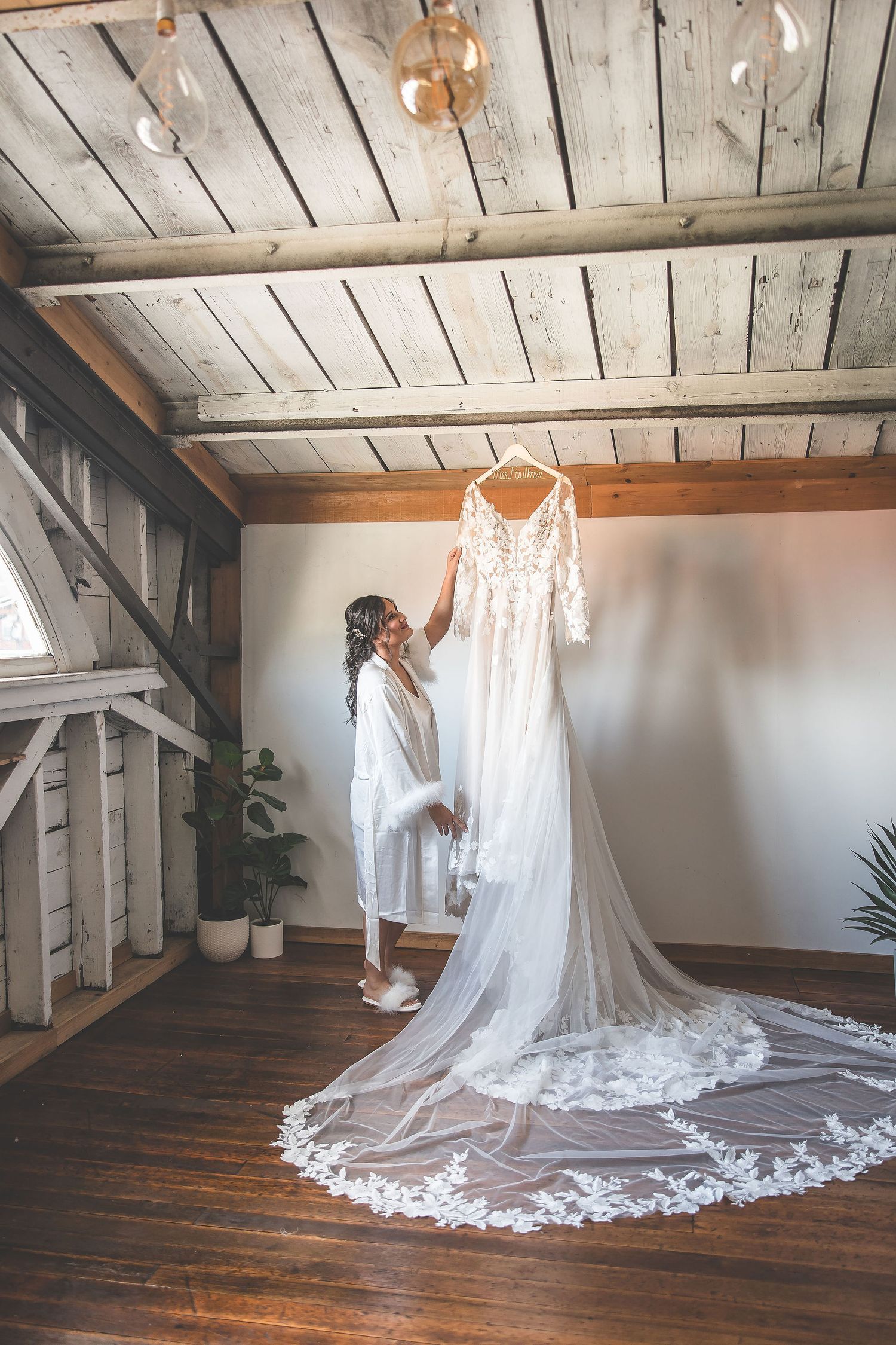 A stunning lace wedding dress with long train displayed in a rustic room with wooden floors and ceiling.