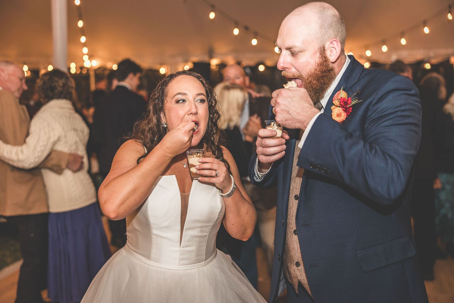 Wedding guests dancing and celebrating during an evening reception under romantic string lighting.