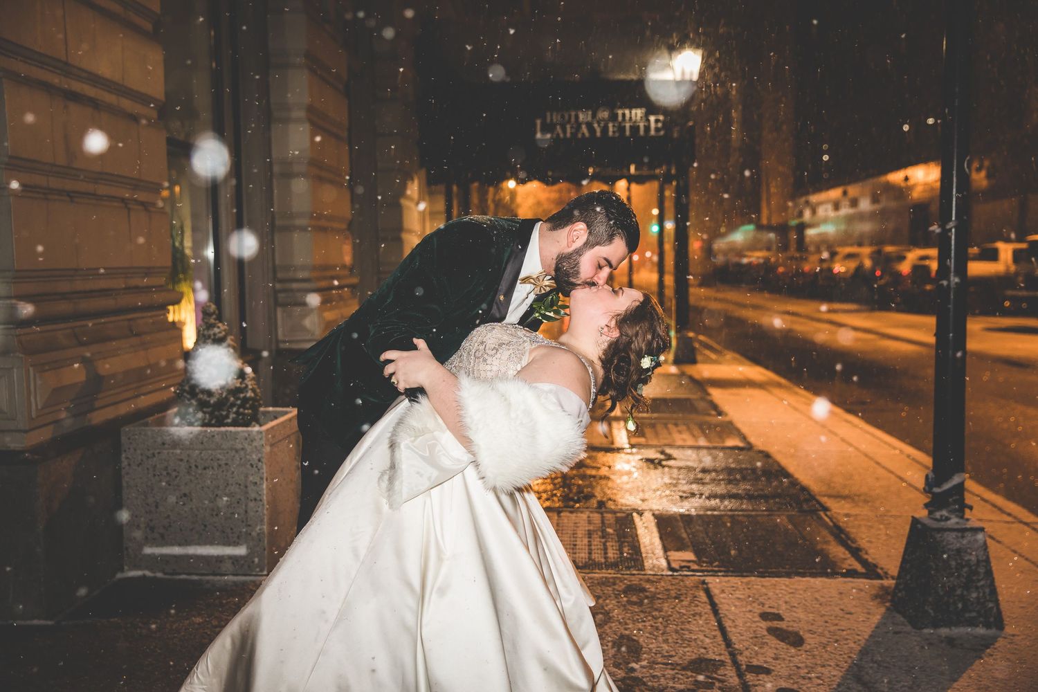 Nighttime winter wedding scene with falling snow and illuminated building exterior.