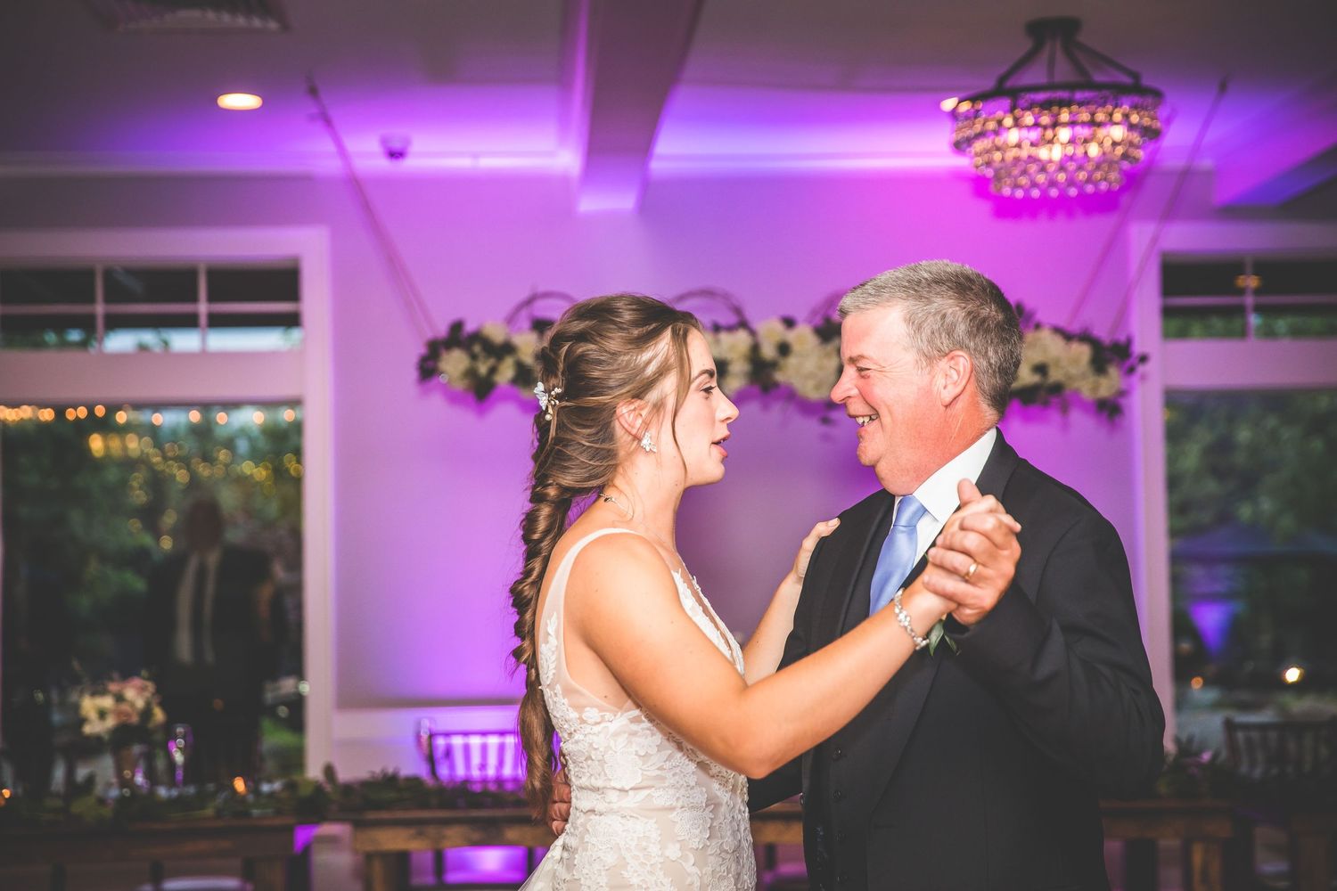 Couple dances together in an elegant ballroom with purple ambient lighting and chandeliers.