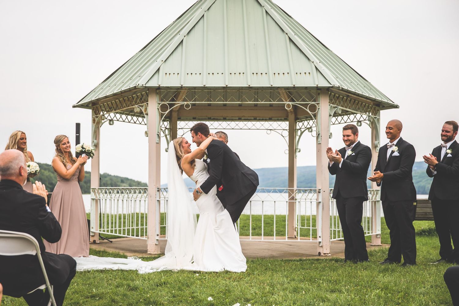Wedding ceremony setup with white gazebo and folding chairs overlooking a scenic waterfront.