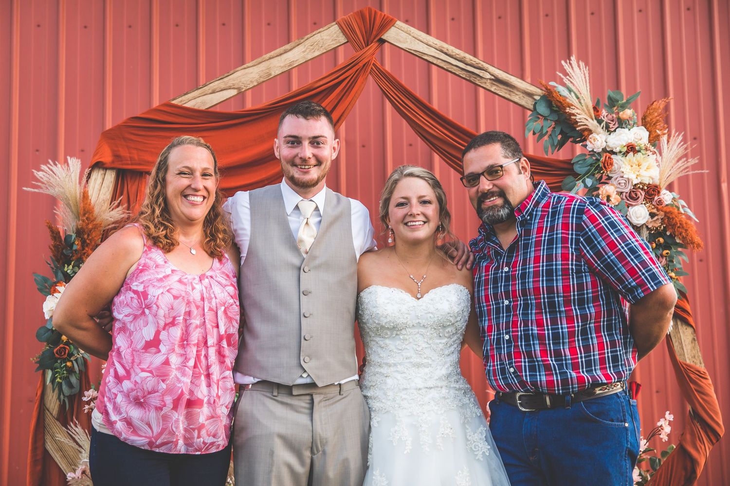 Wedding party posing in front of a red barn wall wearing coordinated pink and navy outfits.