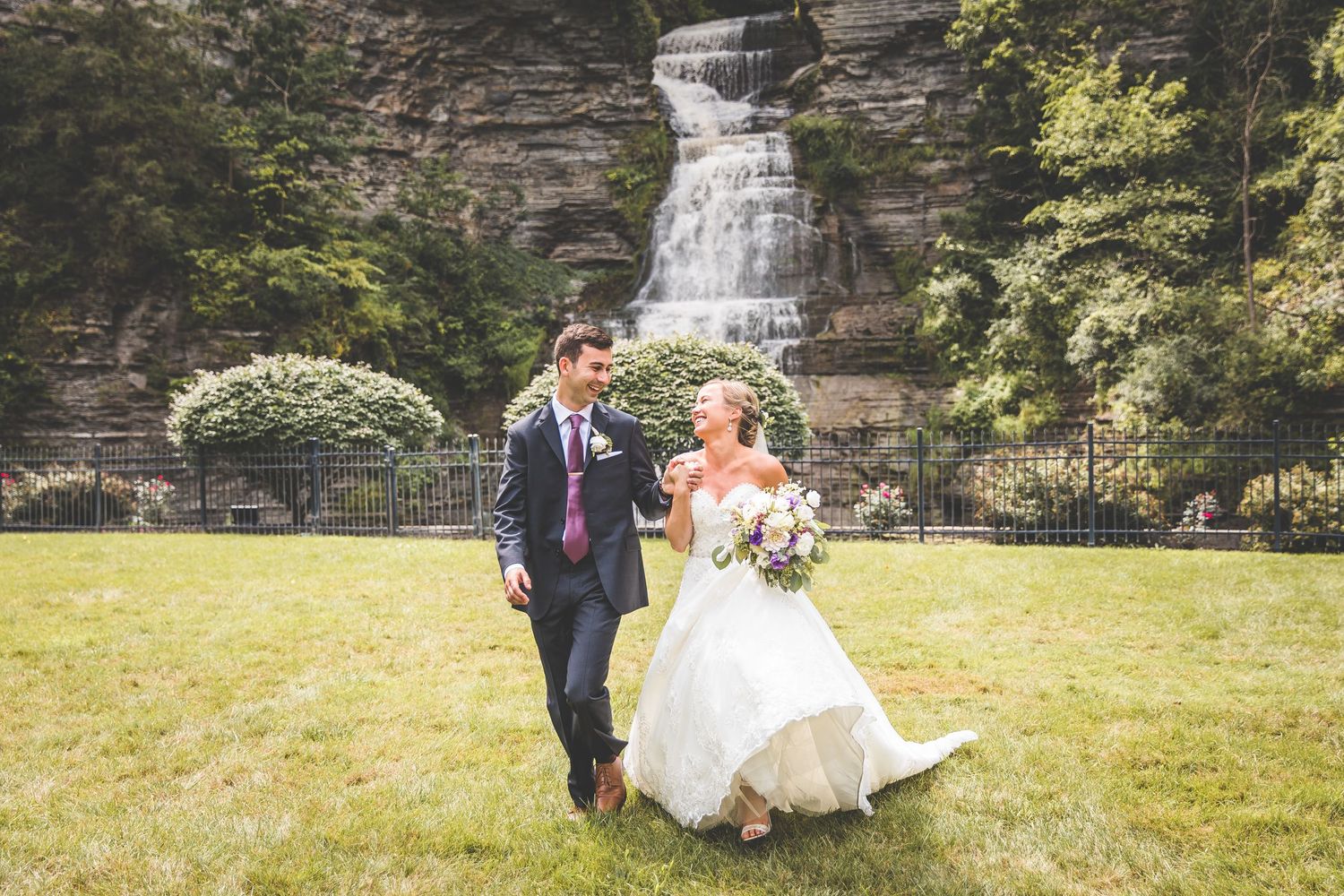 Wedding couple relaxing by stone waterfall in garden setting.