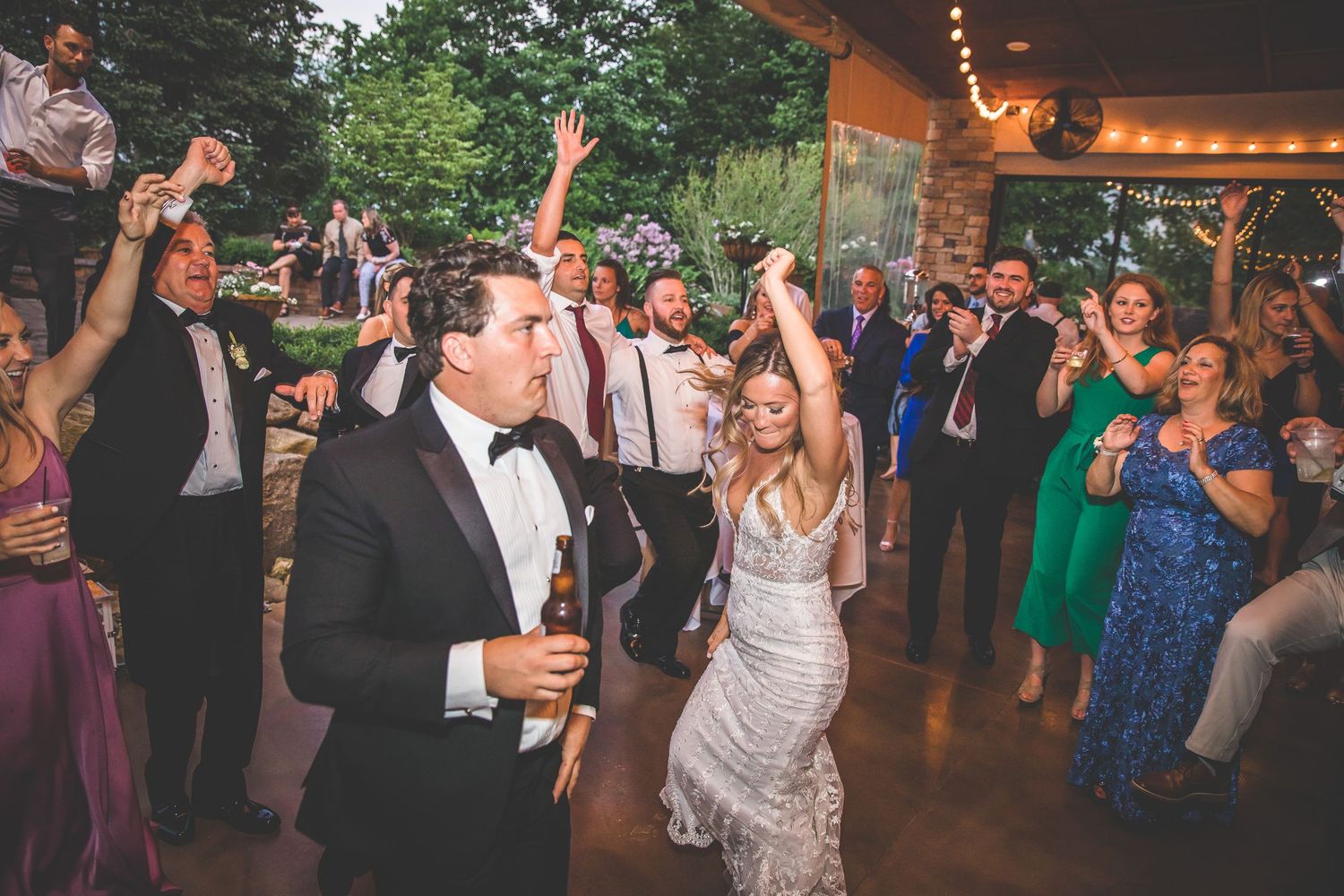 Wedding celebration with guests dancing under string lights at an indoor-outdoor venue.