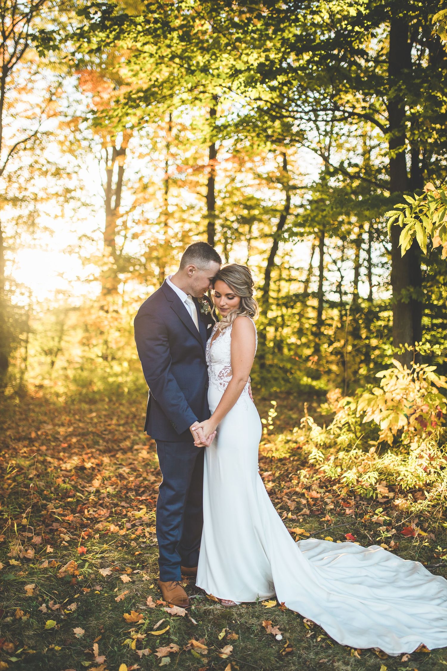 Autumn wedding portraits in a sunlit forest with golden leaves and long flowing white dress.