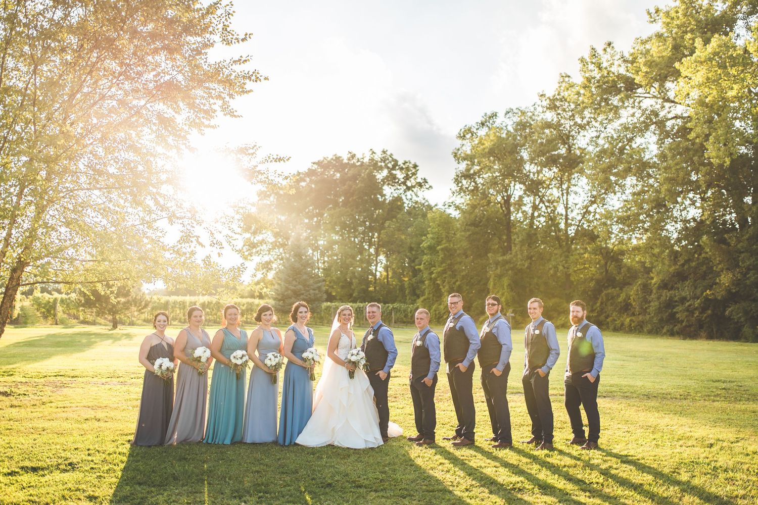 Wedding party lined up at sunset in a grassy field with golden sunlight.