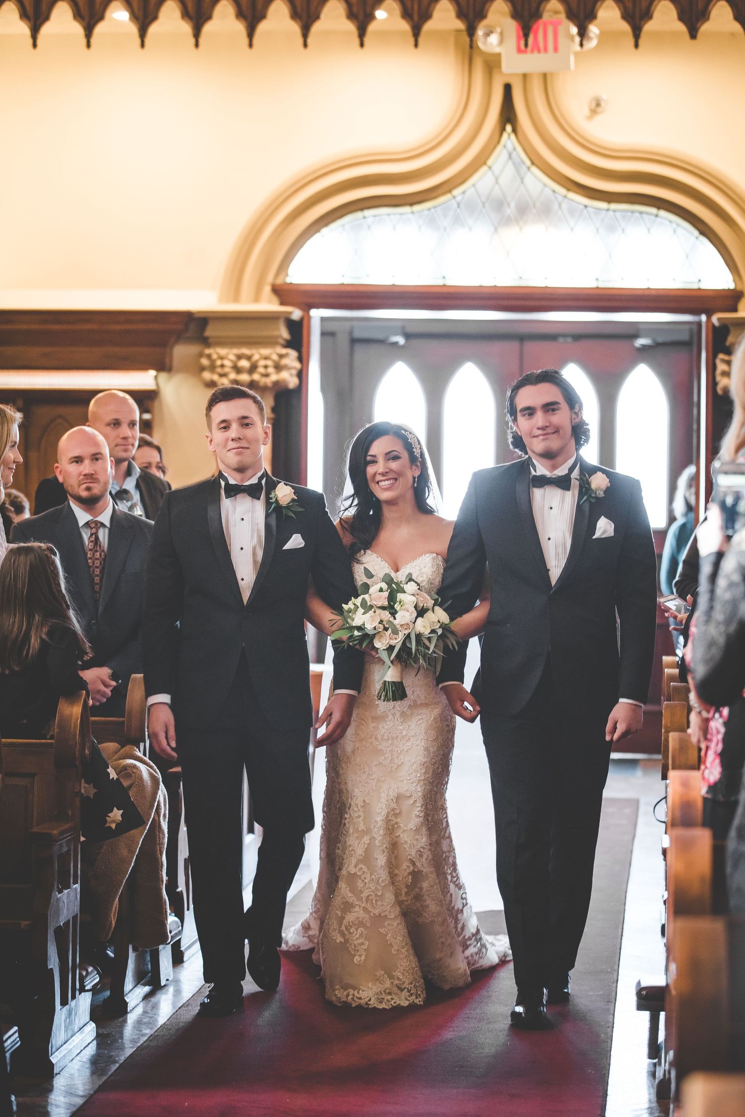 Wedding ceremony processional in a traditional church with ornate gothic architecture and stained glass windows.