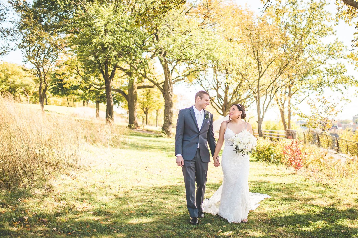 Wedding couple walking through sunlit autumn trees with golden leaves.