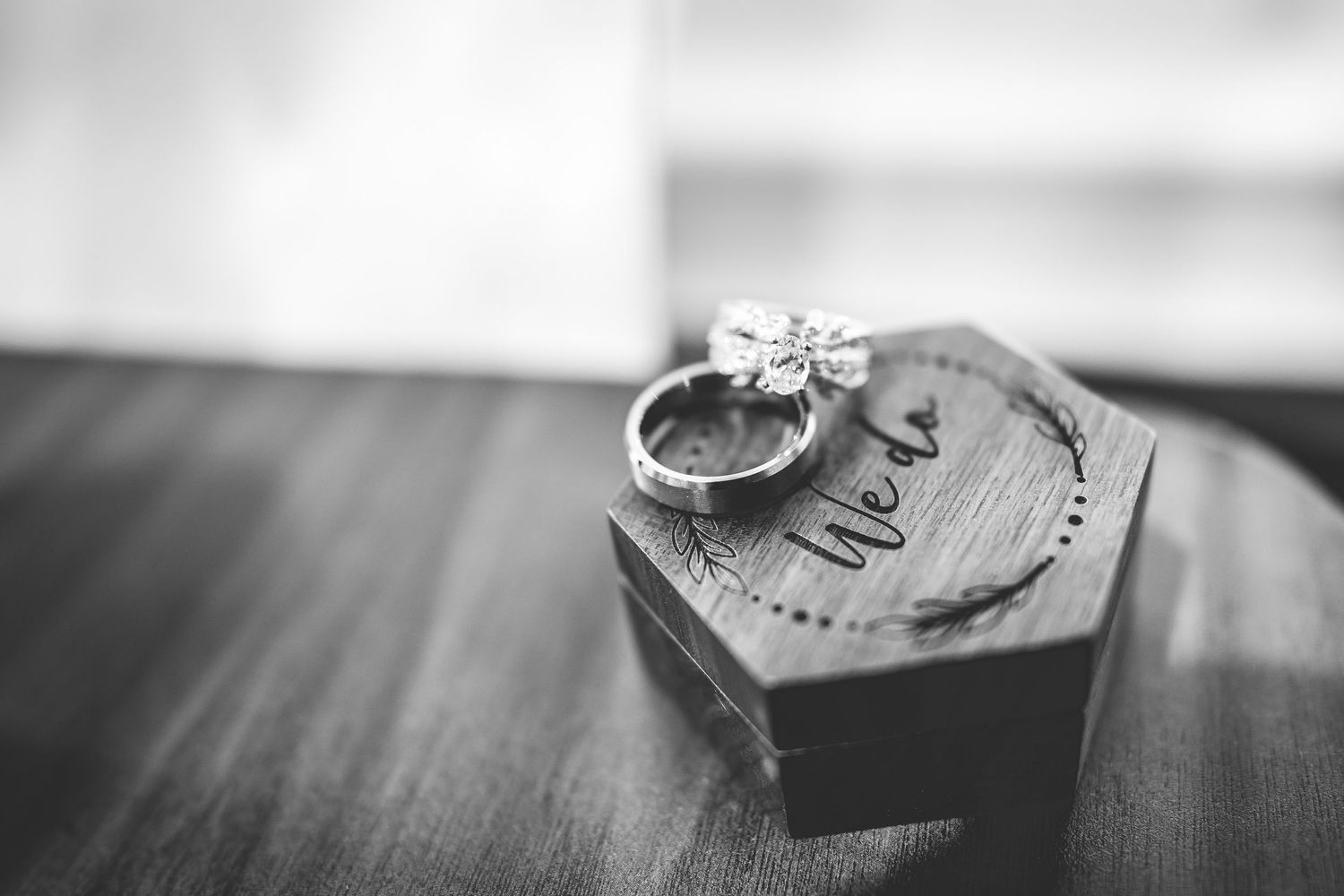 Wedding rings displayed artistically in black and white on wooden surface.