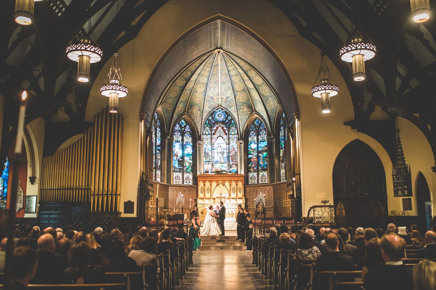 Panoramic view of a church wedding ceremony with guests seated in wooden pews.