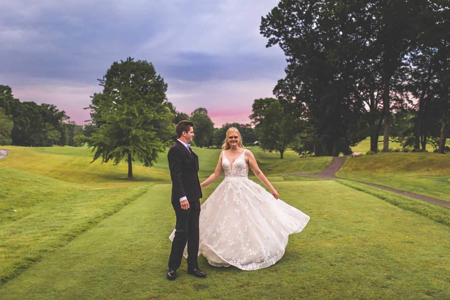 Couple twirls in an elegant dance pose on manicured golf course grounds.