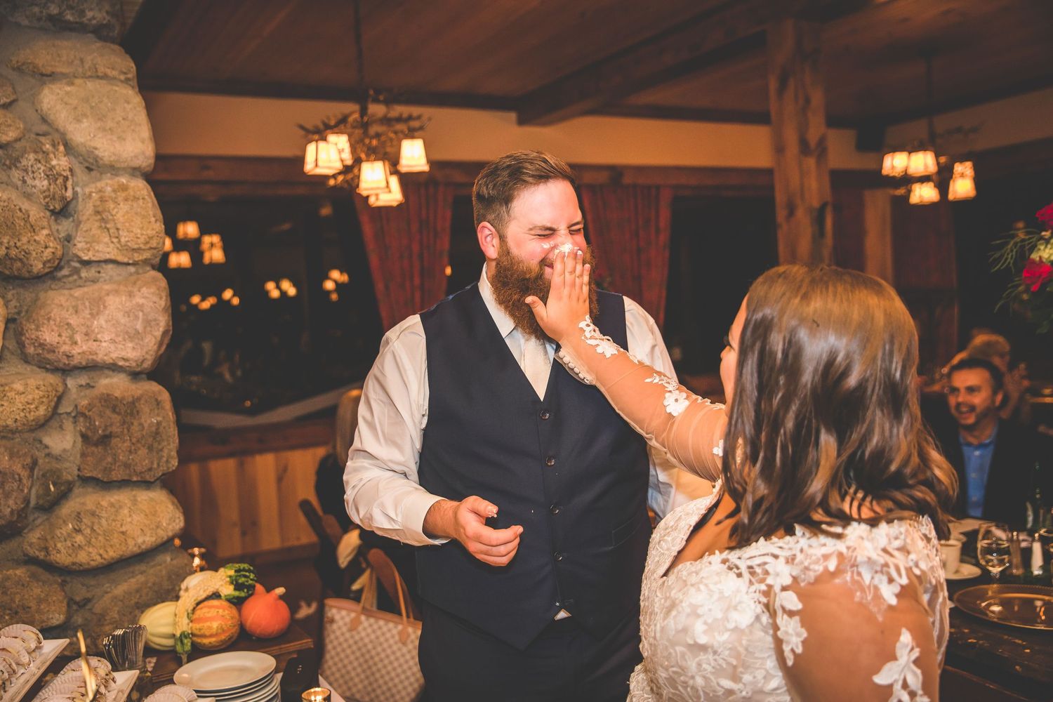 Couple shares playful cake-cutting moment at rustic wedding reception with stone walls and warm lighting.