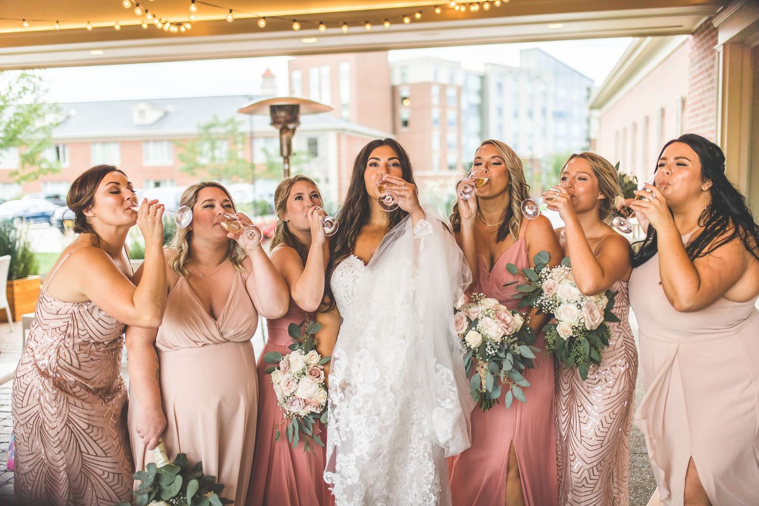 Bridesmaids in pink dresses pose playfully with bride for candid wedding photo.