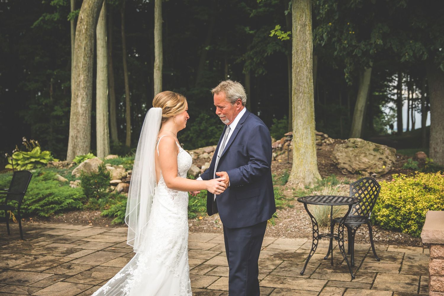 Couple sharing a moment on stone patio surrounded by tall trees.